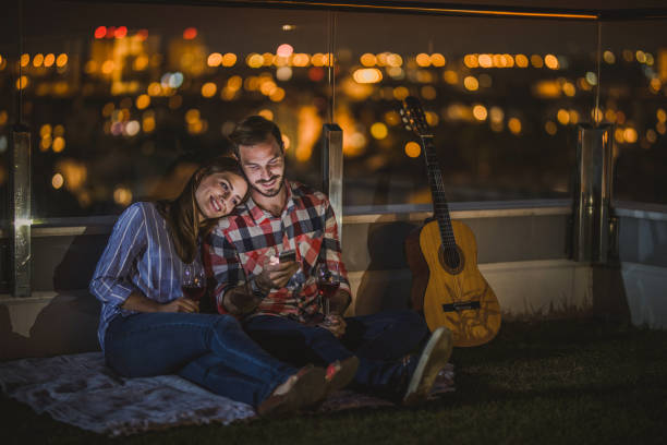 istock Young couple using smart phone on a penthouse terrace by night. 871900624