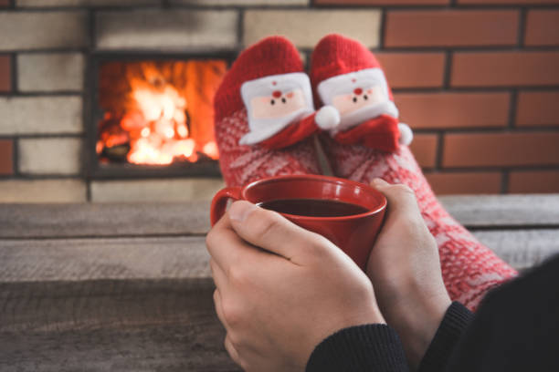 tazza di caffè rosso in mano femminile vicino al camino. la femmina si rilassa scaldando con i calzini rossi di natale. vacanze di natale. - brick red wool heat foto e immagini stock