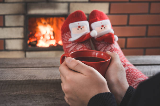czerwona filiżanka kawy w kobiecej dłoni przy kominku. kobieta relaksuje się przez ciepły ogień w świątecznych czerwonych skarpetkach. święta bożego narodzenia. - brick red wool heat zdjęcia i obrazy z banku zdjęć