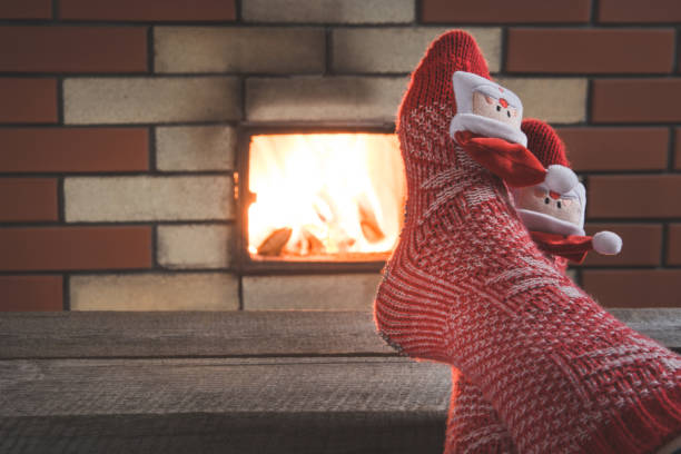 piedi in calze rosse di lana vicino al camino. da vicino in piedi. tavolo per visualizzare il prodotto natalizio. - brick red wool heat foto e immagini stock