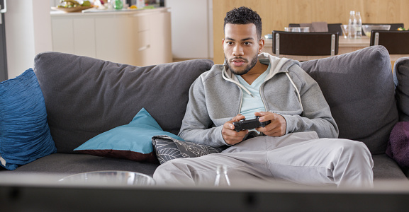 Young man sitting on sofa in living room and playing video game.