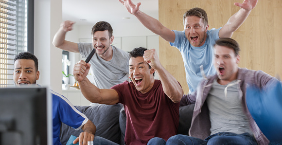 Friends watching football match on TV and celebrating a goal.