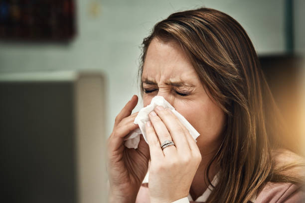 istock Blonde woman seated at computer sneezes, blows her nose 871923260