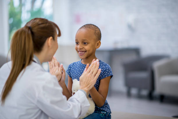 Checkup bem-sucedido Uma médica caucasiana e uma jovem de ascendência africana estão dentro de um quarto de hospital. A menina tem câncer. Ela está sorrindo e dando um high-five para seu médico. leucemia stock pictures, royalty free photos & images