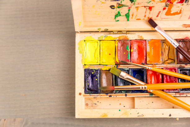 Paints for drawing, palette and brush on a wooden background
