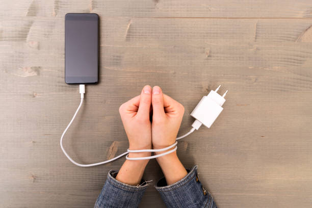 las manos femeninas y smartphone. manos de mujer atrapada y envuelven en muñecas con cable de teléfono móvil como esposas. adicción a internet y redes sociales - malos hábitos fotografías e imágenes de stock