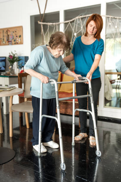 istock Assistant in Retirement Home Helping Senior Woman Walking with Mobility Walker 871947550