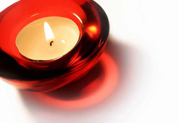 Burning candle in red glass candlestick close-up on white background