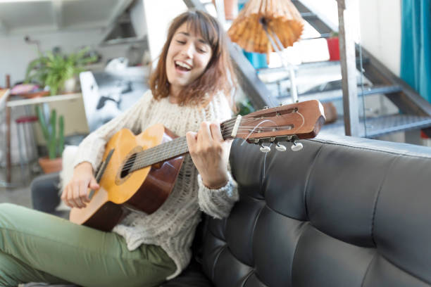 istock Beautiful woman sitting on a sofa and  playing guitar 871962996