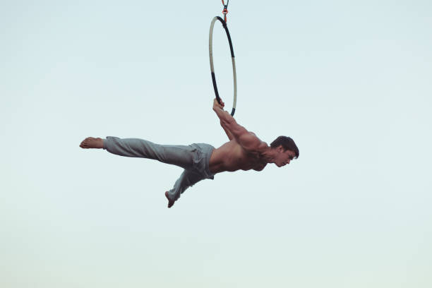 Man is an acrobat high in the sky. Man is an acrobat high in the sky, he shows the performance on the ring. acrobatic activity stock pictures, royalty-free photos & images