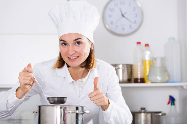 Smiling female cook checking taste of food while preparing in kitchen