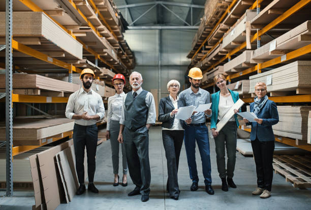 Industrial design team in a meeting. Closeup front view of mixed age people of industrial design department at a factory. They are standing in an aisle between pallet racks stacked with chipboard, MDF and plywood. There are three men and three women. manufacturing occupation photos stock pictures, royalty-free photos & images