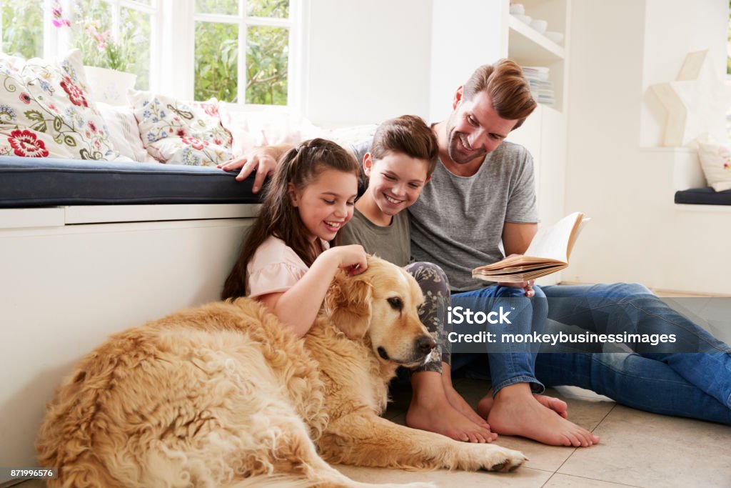 Father Reading Book With Son And Daughter And Pet Dog At Home Family Stock Photo