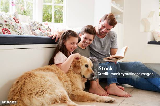 Father Reading Book With Son And Daughter And Pet Dog At Home Stock Photo - Download Image Now