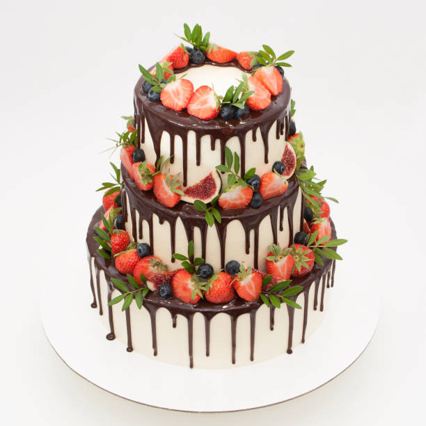 istock Three-tiered wedding cake in chocolate, decorated with slices strawberries, blueberries, figs and green leaves. 872001096