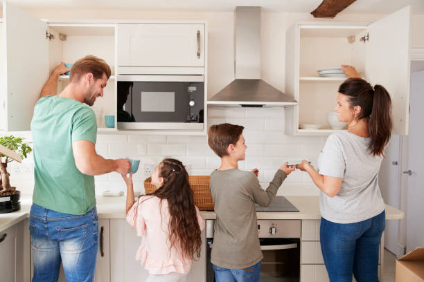 Children Helping To Put Away Crockery In Kitchen Cupboards