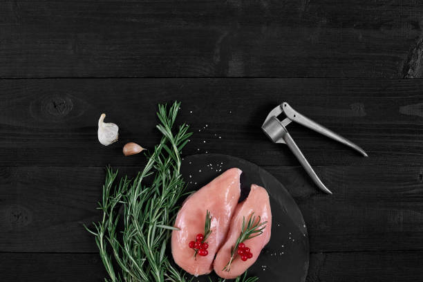 chicken breast on a cutting board with herbs, spices and garlic press on rustic wooden background - garlic chicken breast raw chicken imagens e fotografias de stock