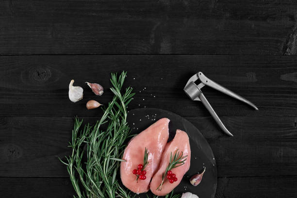 chicken breast on a cutting board with herbs, spices and garlic press on rustic wooden background - garlic chicken breast raw chicken imagens e fotografias de stock