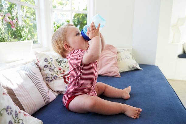 istock Baby Boy Sitting On Seat By Window Drinking From Training Cup 872016502
