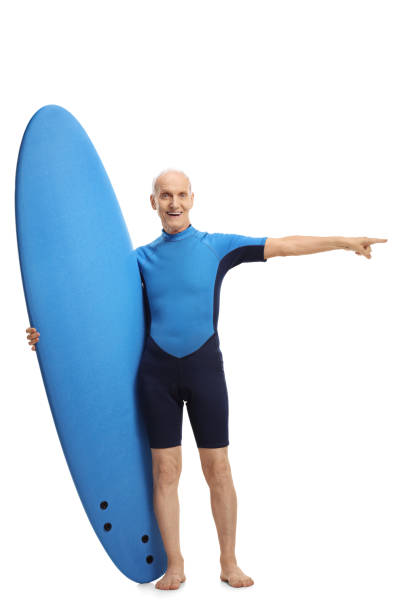 istock Senior in a wetsuit holding a surfboard and pointing 872016856