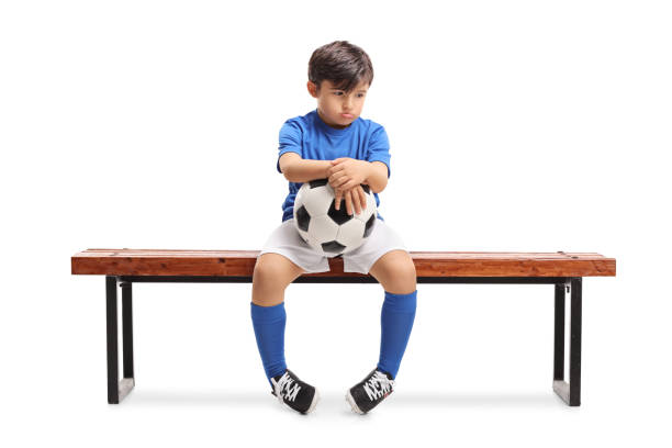 traurige kleine fußballer sitzt auf einer holzbank - little boys child sadness depression stock-fotos und bilder