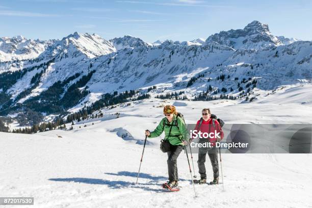 Photo libre de droit de Couple De Personnes Âgées Est La Randonnée En Raquettes Dans La Montagne Alpine Hivernale Bavière Allemagne banque d'images et plus d'images libres de droit de Raquette à neige