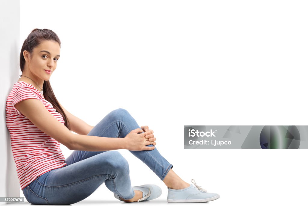 Teenage girl sitting on the floor and leaning against a wall Teenage girl sitting on the floor and leaning against a wall isolated on white background Adolescence Stock Photo