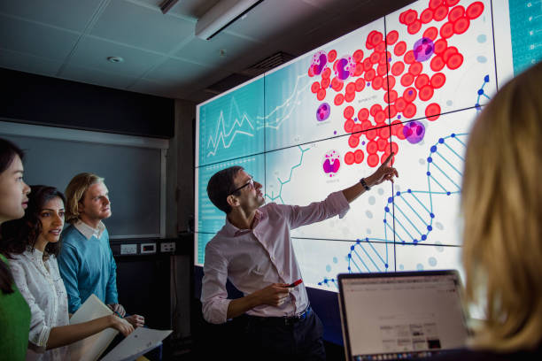 Learning about DNA Phenotyping Group of business professionals in a dark room standing in front of a large data display screen with information. innovation technology stock pictures, royalty-free photos & images