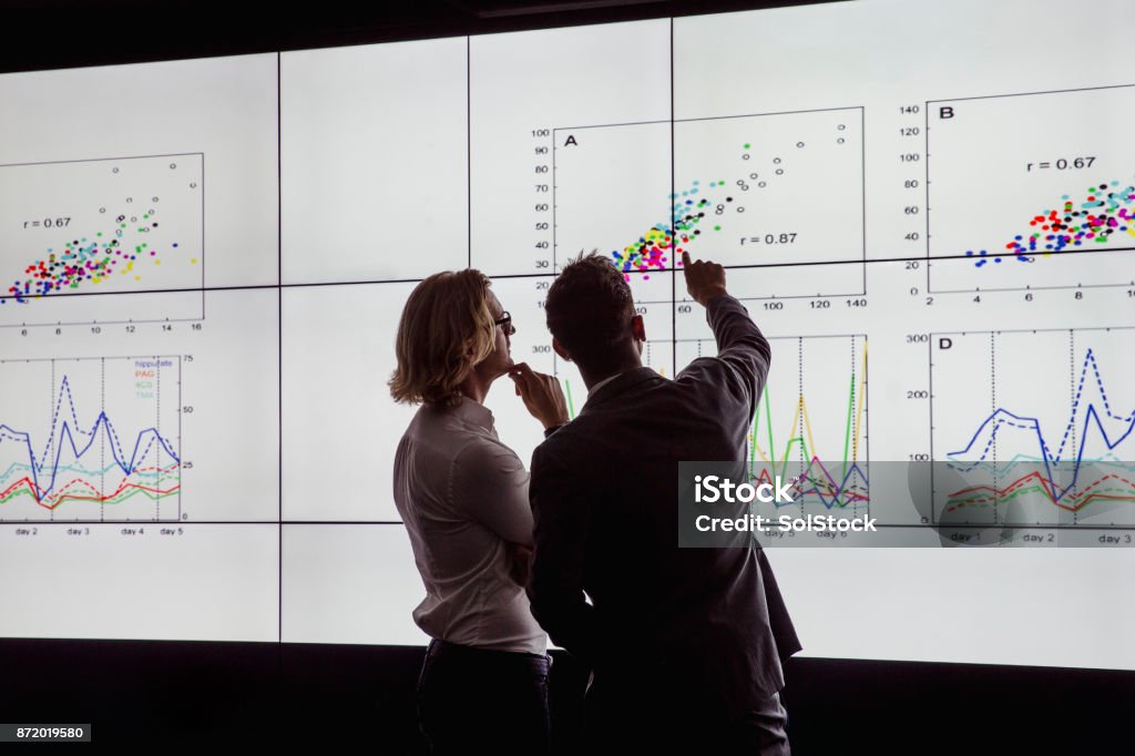Men Viewing a Large Screen of Information Business men in a dark room standing in front of a large data display Data Stock Photo