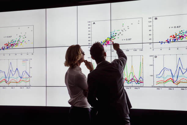 Men Viewing a Large Screen of Information Business men in a dark room standing in front of a large data display research stock pictures, royalty-free photos & images