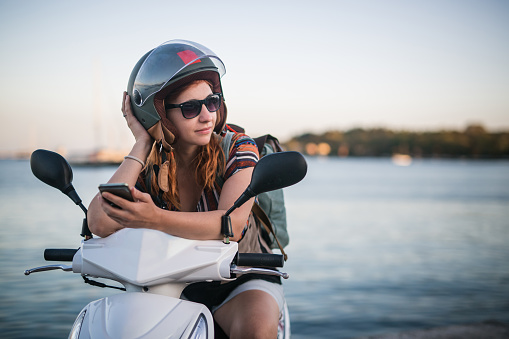 Young independent woman on journey, sitting on her motorcycle, taking a rest from ride next to the sea