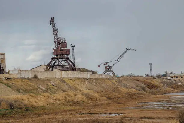 Consequences of Aral sea ecological catastrophe. Abandoned port with rusty cranes on the shore of dried Aral sea.