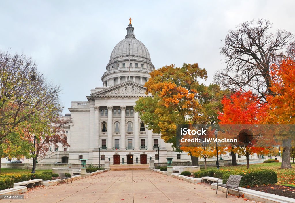 Wisconsin State Capitol building National Historic Landmark city of Madison, Wisconsin, Midwest USA. Autumn view with bright colored trees along path to the entrance and cloudy sky during later afternoon. Wisconsin Stock Photo