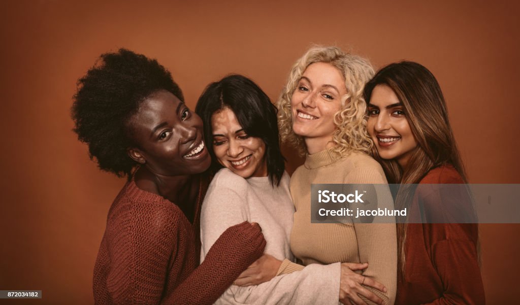 Group of cheerful young women standing together Group of cheerful young women standing together on brown background. Multi ethnic female friends in studio. Women Stock Photo