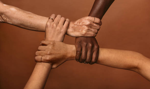 Unity in diversity Four diverse women holding each others wrists in a circle. Top view of female hands linked in the lock against brown background. responsibility photos stock pictures, royalty-free photos & images