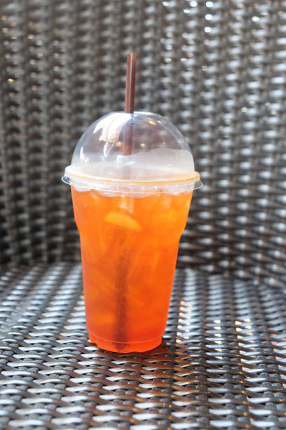 Cold iced tea with lemon and straw in takeaway plastic cup on wicker table
