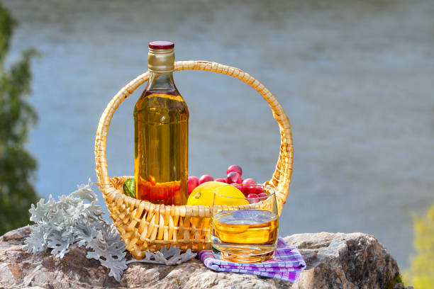 bottiglia con il bicchiere di whisky e il cesto con frutta sulla roccia vicino a un fiume - gin decanter whisky bottle foto e immagini stock