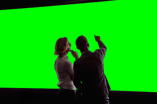 Group of business professionals in a dark room standing in front of a large data display green-screen