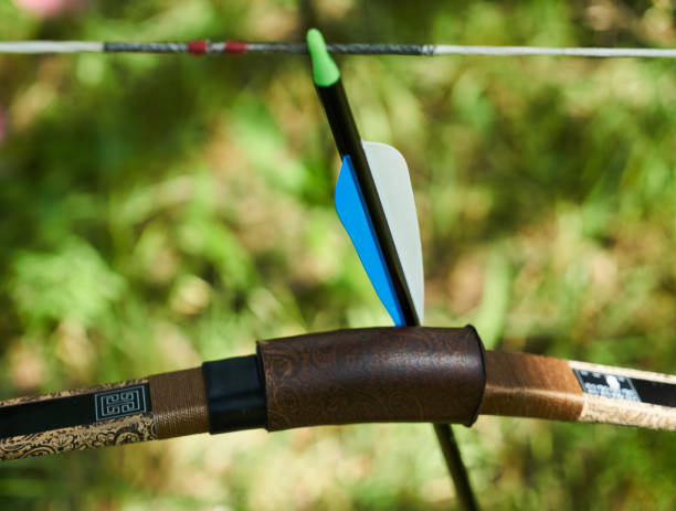 istock Archery bow and arrow with colorful feather on green blurred forest background, close-up 872077476