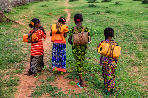 African girls from Borana tribe carrying water to the village, African women and children often walk long distances to bring back jugs of water that they carry on their back.\n