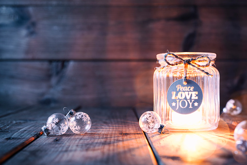 Cute christmas decoration with a light in a jar and some christmas ornaments. Jar is decorated with a bow and a label showing the words Peace, Love, Joy.