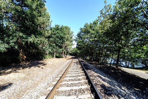 Perspective view of a train track in current use in Galicia (Spain) with a lot of vegetation on the sides of the track and the blue sky and totally clear