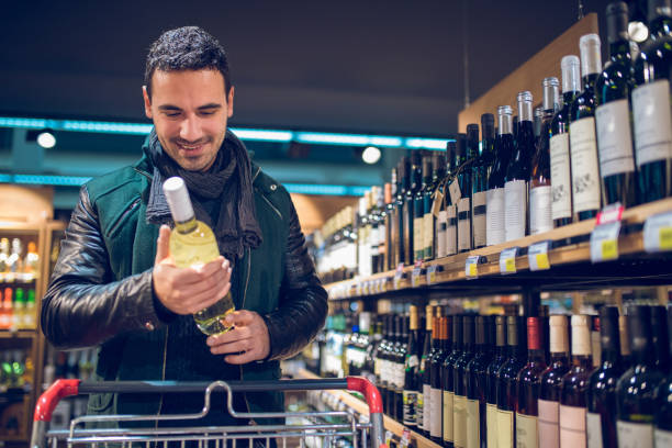istock Young man in a supermarket choosing wine 872116594