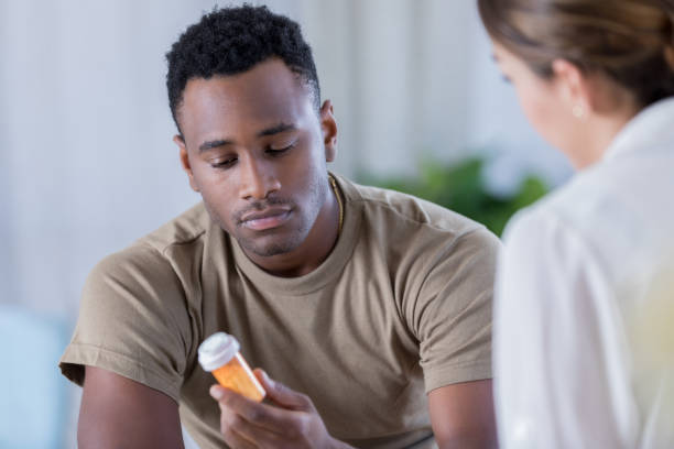 Young military officer receives medication for depression A young African American male military office sits across from his unrecognizable therapist and reads a prescription bottle.  His therapist has prescribed the medication for his depression. pill bottle photos stock pictures, royalty-free photos & images