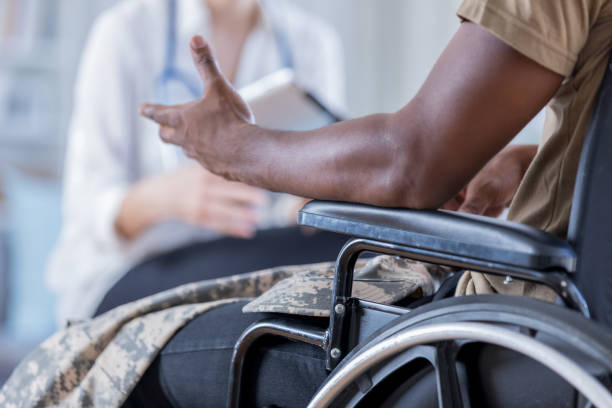 Unrecognizable wounded warrior discusses symptoms with doctor In this closeup, both a doctor and military patient are unrecognizable as the patient shares his symptoms.  Focus is on the wheelchair bound officer as he gestures during the discussion. black military man stock pictures, royalty-free photos & images