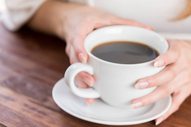 A lovely young blonde woman pouring coffee smiles up at the camera.