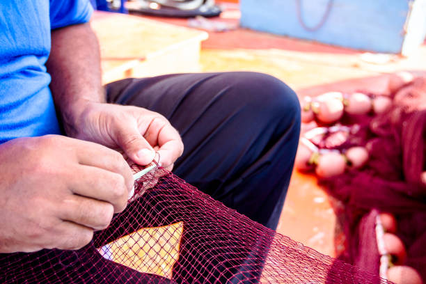 Old fisherman tying up his orange color fishing net with his old and wrinkled hands against dark orange color and light blurred background.
