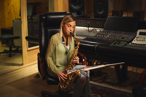 Young female musician playing saxophone in a music studio.