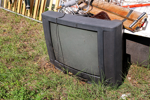 Old TV set dumped and left in the garden along with other bulky trash. Old TV thrown away next to a wall with a pile of mixed garbage in natural environment. Recycling industry. Not Ecology. Ecology.