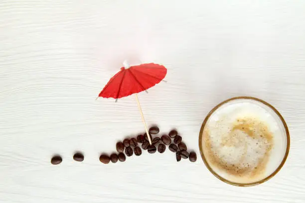 frothy latte beside red umbrella and beans top view